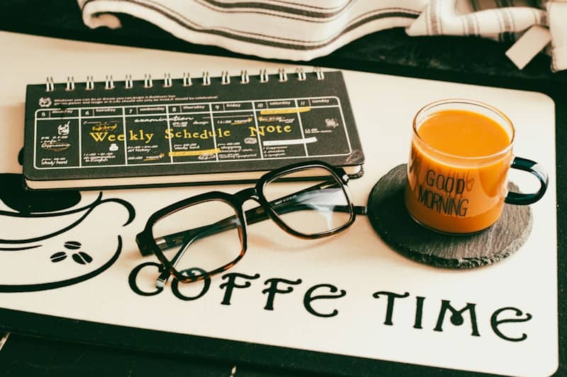 Glasses, coffee mug, and planner on a desk.