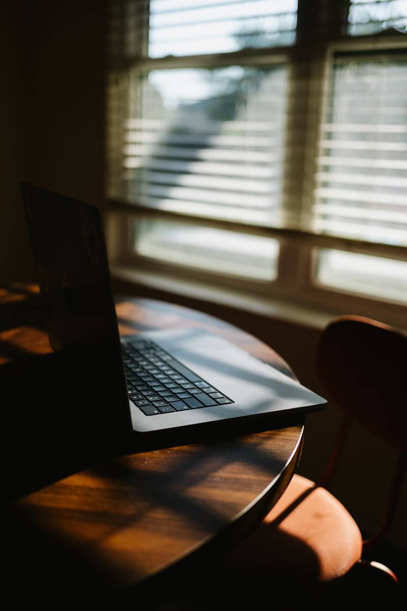 Laptop on a wooden table near a window