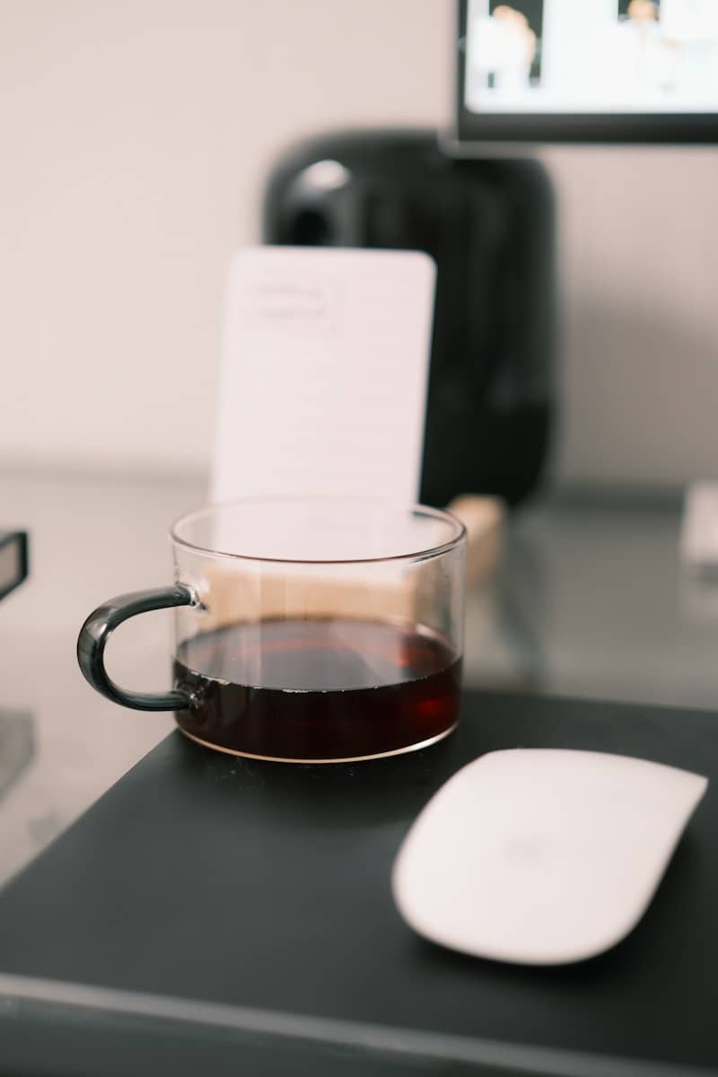 A clear mug of dark coffee sits on a desk.