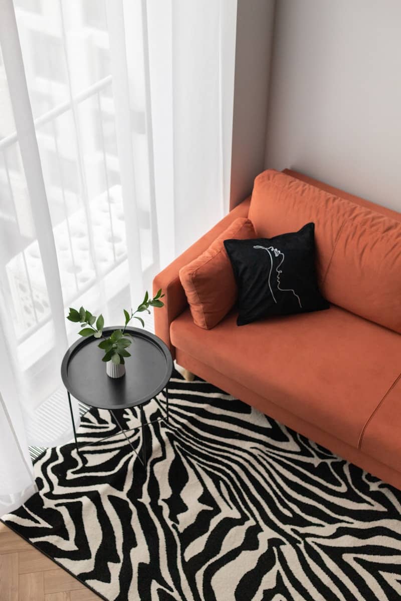 Orange sofa with zebra print rug and side table.