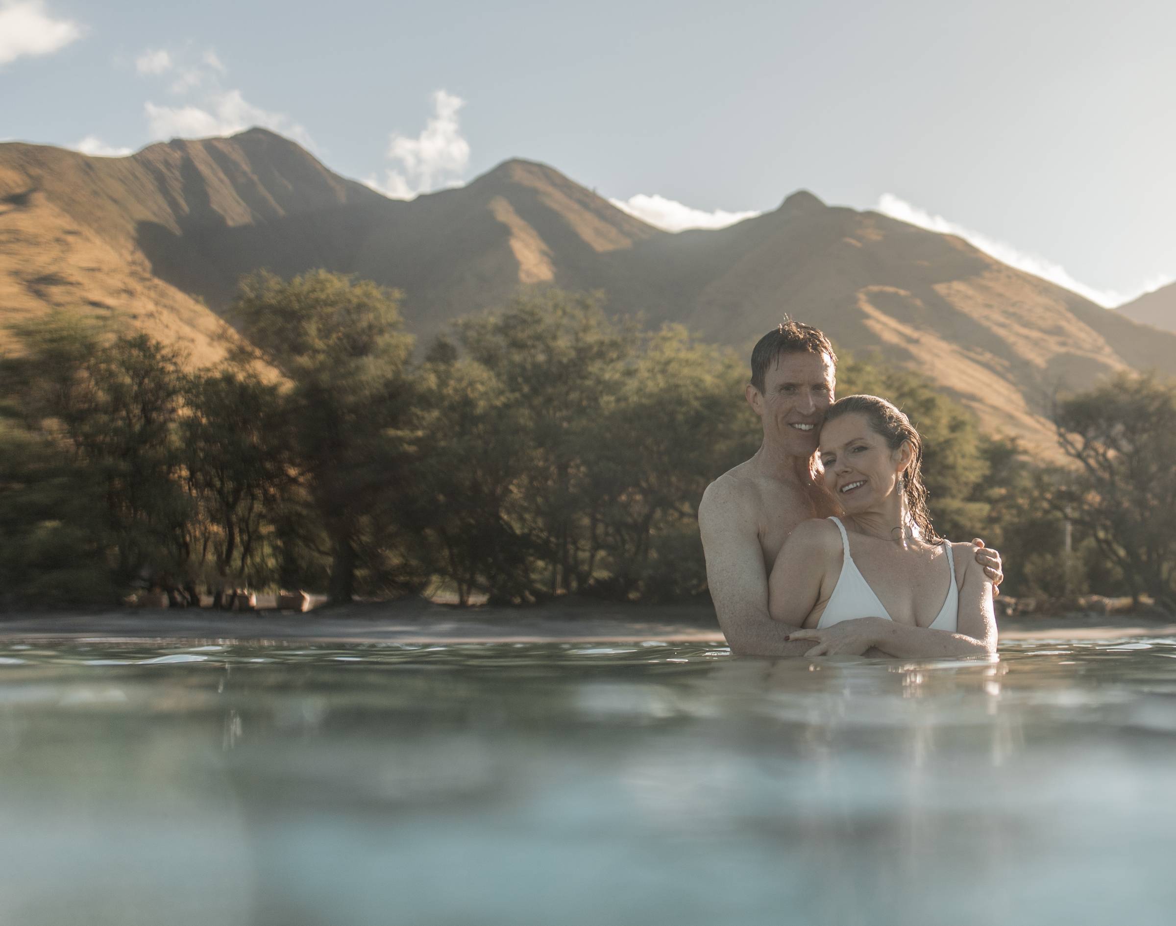 Michele Lisenbury Christensen and husband Kurt embracing in the ocean with mountains in the background