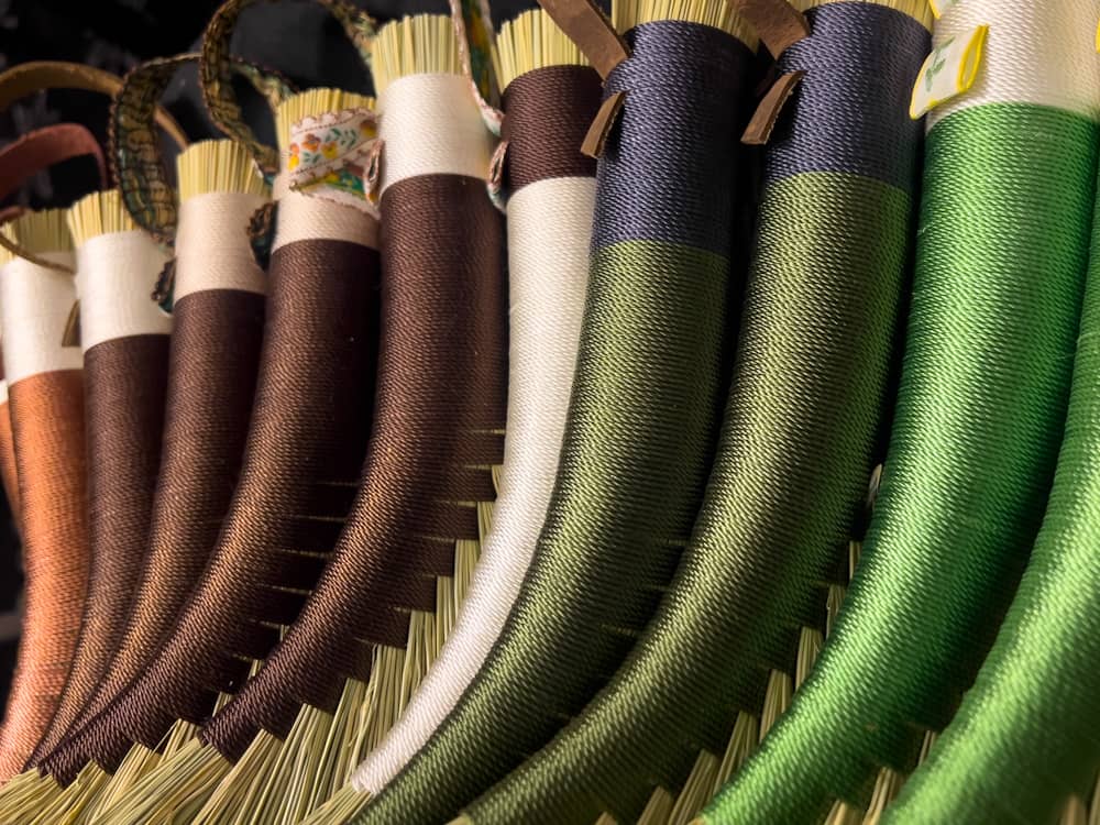 Close-up of several traditional hand brooms with colorful, tightly-wrapped handles in brown, green, and white, displayed in a row.