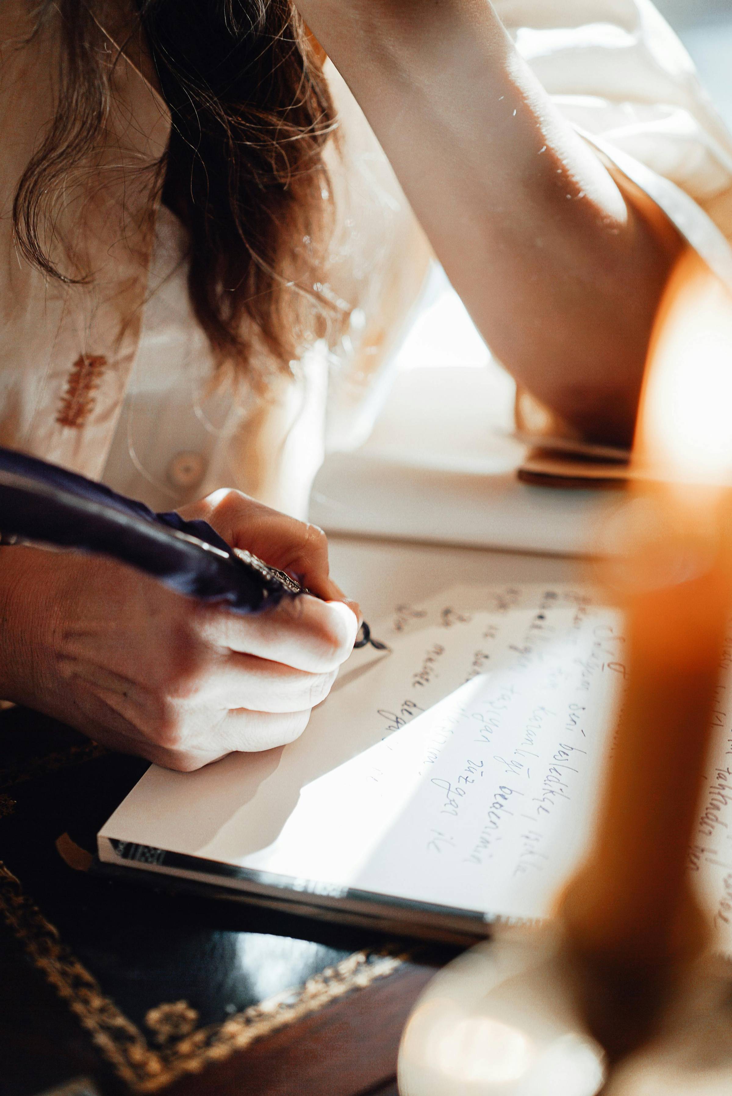 Close-up of a person writing in a notebook with warm sunlight streaming across the page and hand.