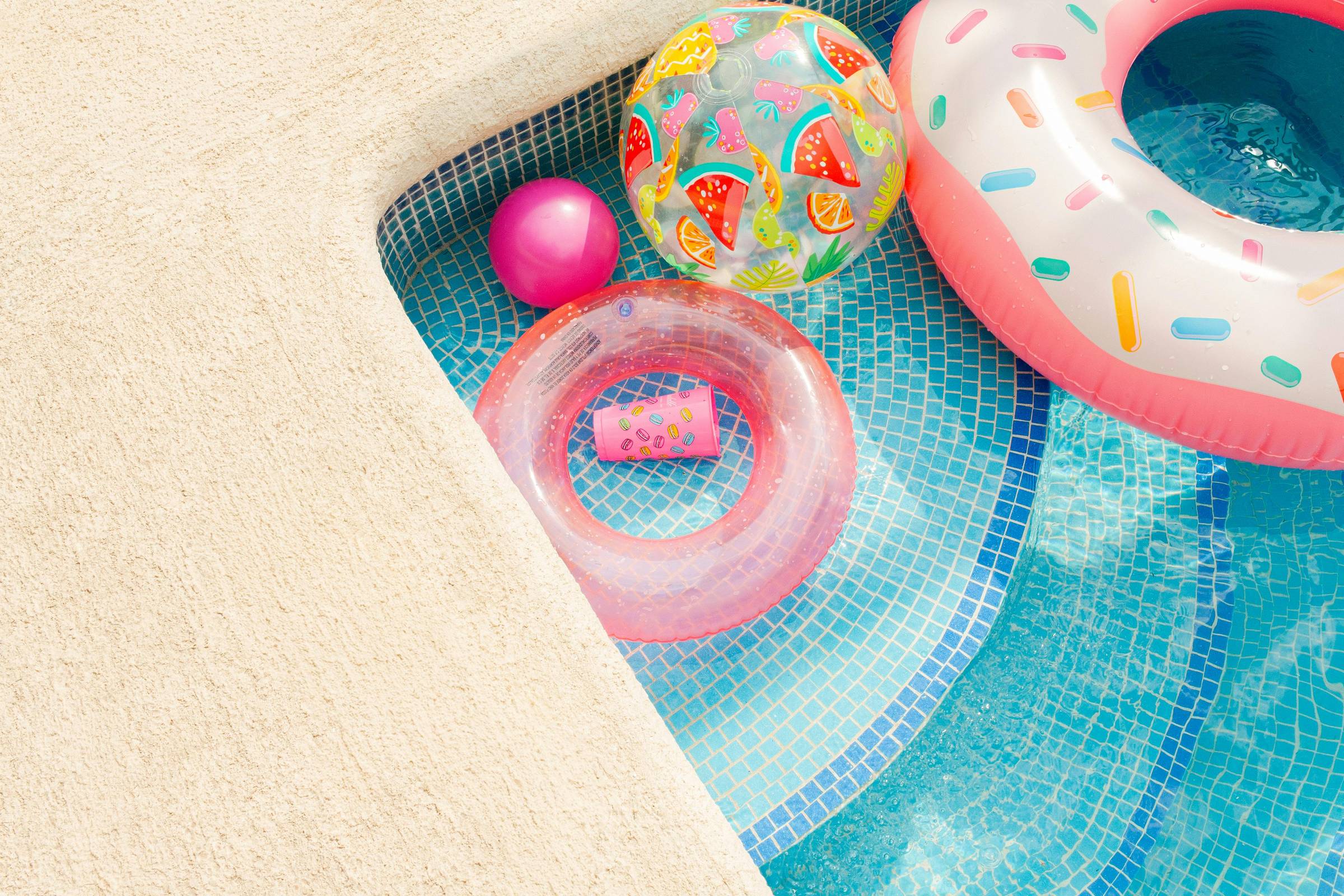 Colorful pool floats and toys arranged beside a bright blue swimming pool on a sunny day.
