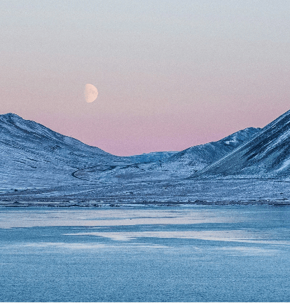 Snowy mountain valley at dusk with a pale moon in a pink and blue sky.
