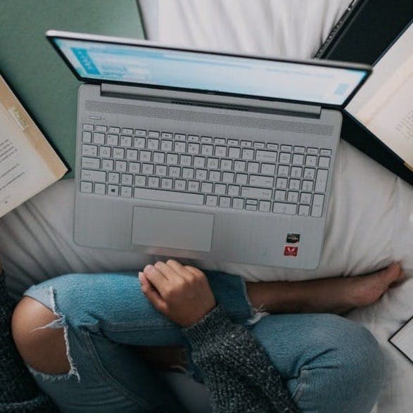 woman in blue long sleeve shirt and blue denim jeans sitting on bed using macbook
