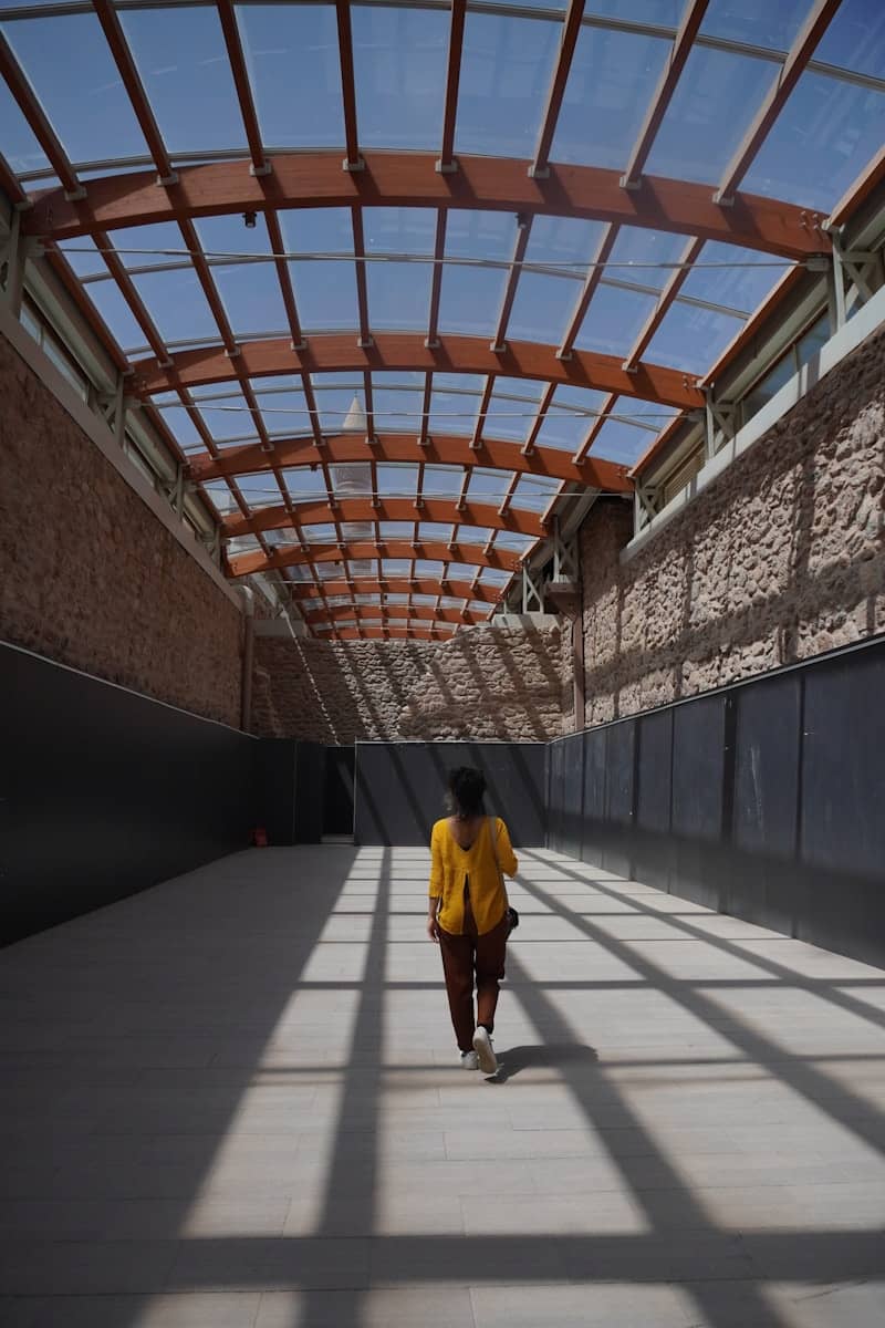 Woman walking down a sunlit corridor with geometric shadows.