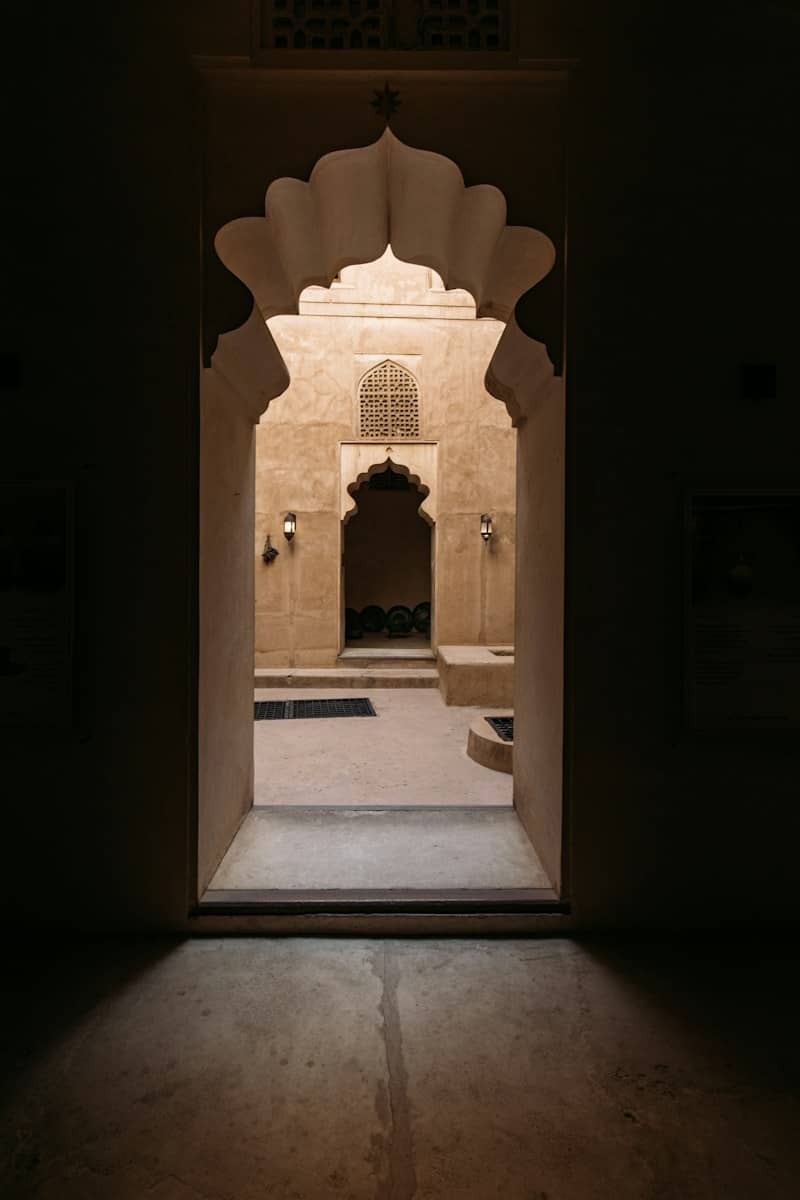 An arched doorway leading to a sunlit courtyard with traditional mud brick architecture