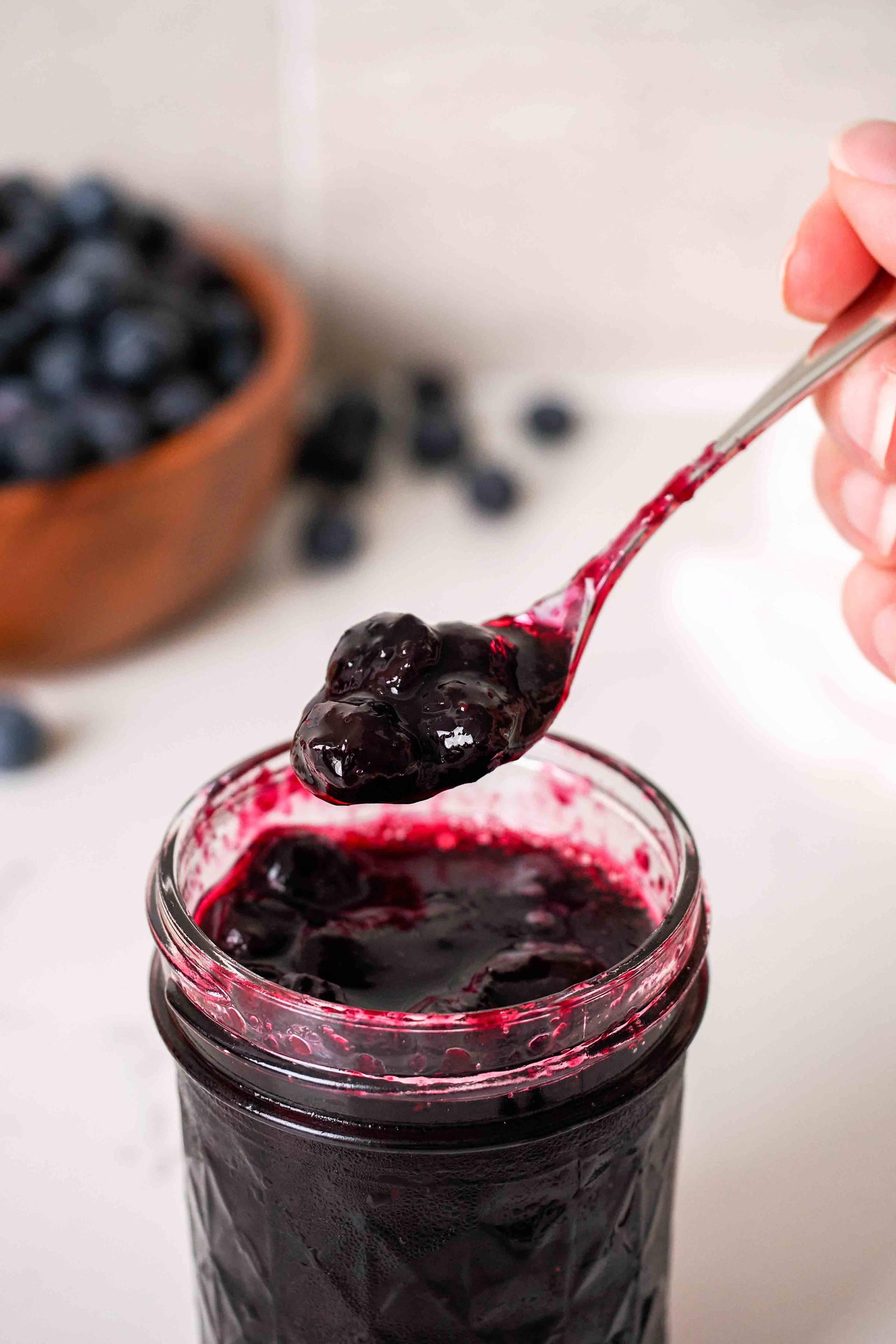 A spoon holds up blueberry jam from a jar
