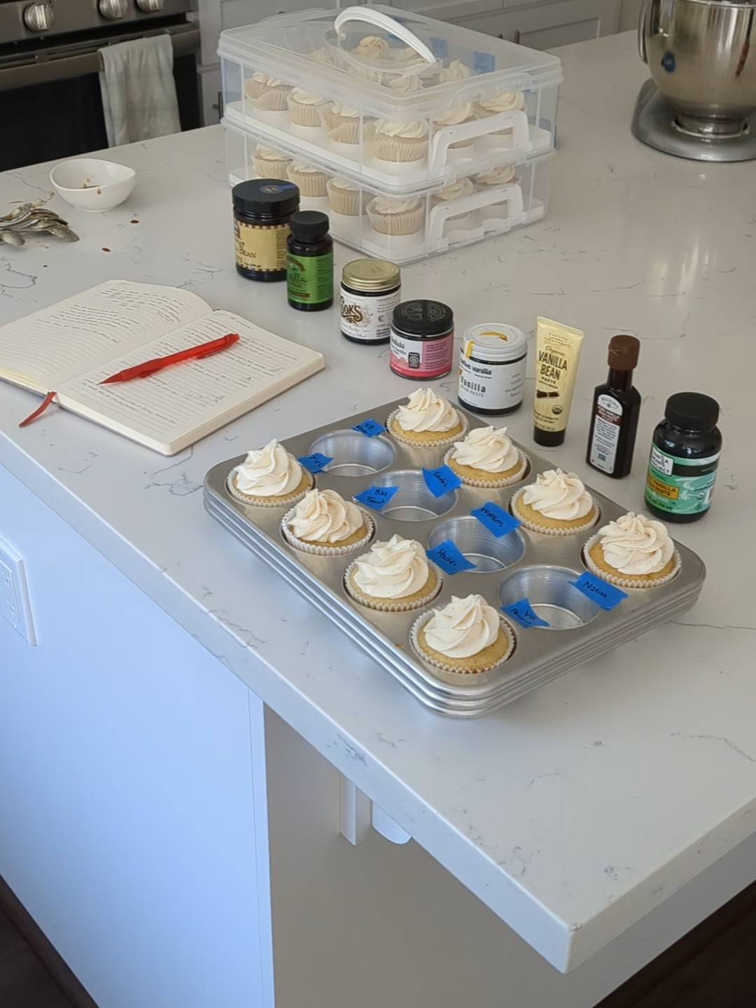 Vanilla cupcakes on a counter with vanilla bean paste bottles.
