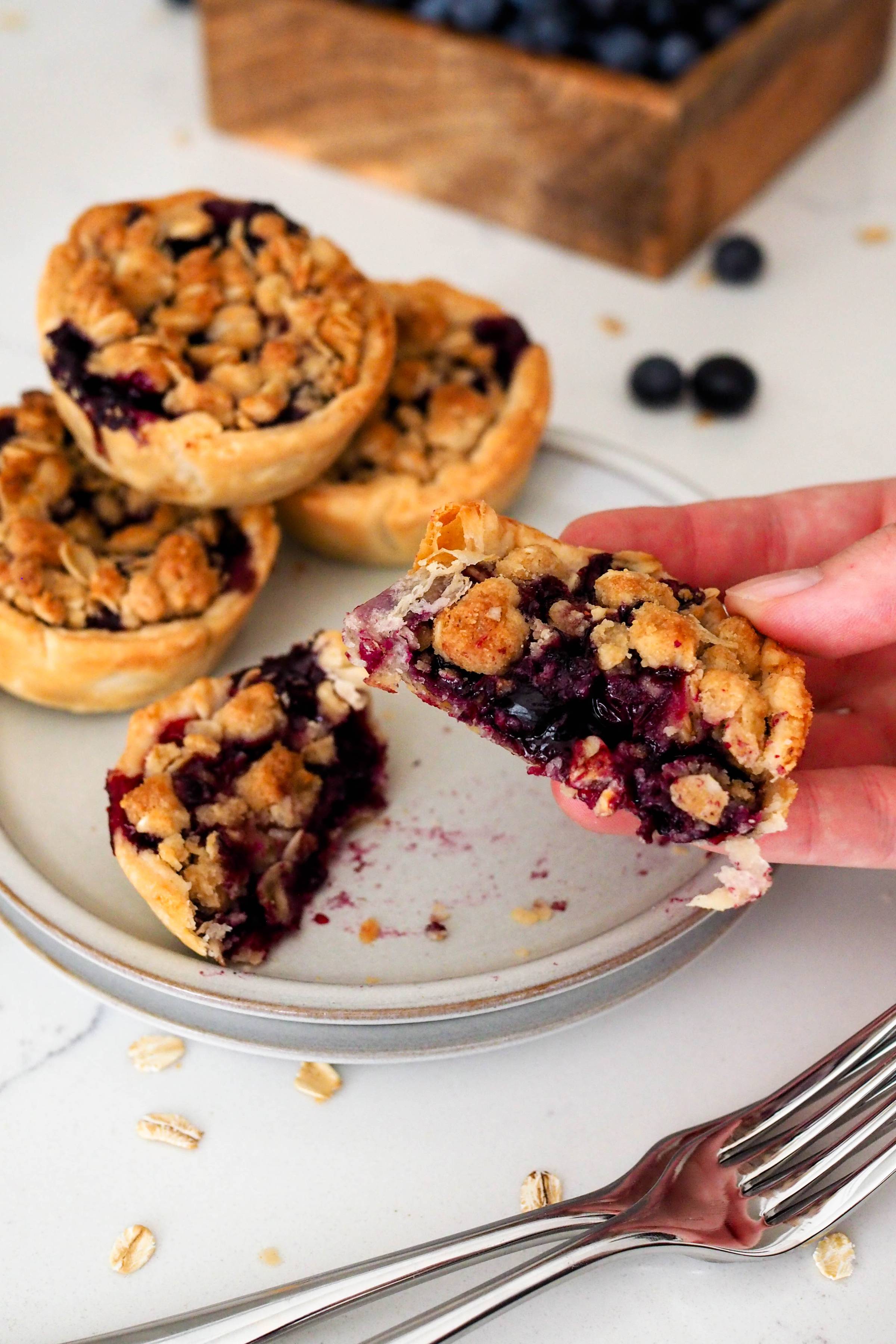 A hand holds up half of a mini blueberry pie.