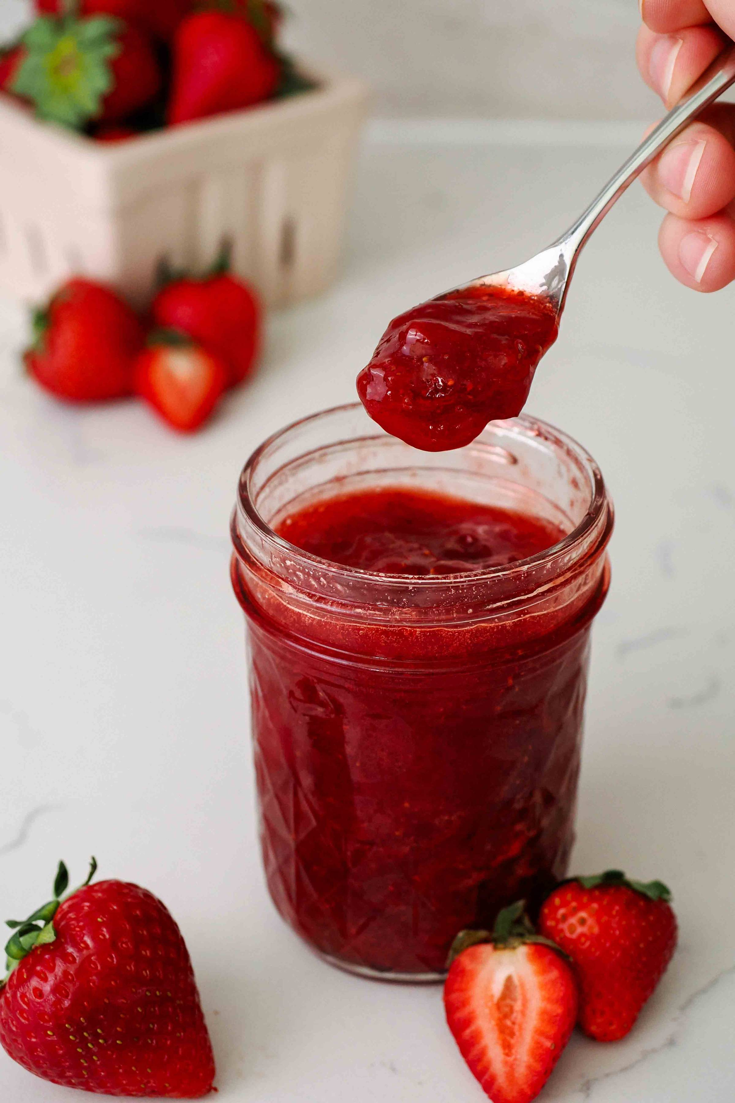 A spoon holds up strawberry jam from a jar