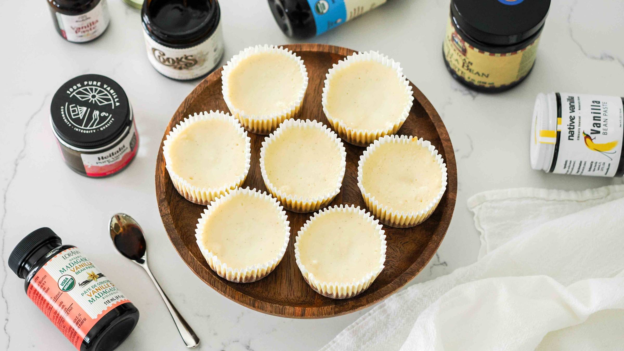 Seven mini vanilla cheesecakes on a wooden cake stand.