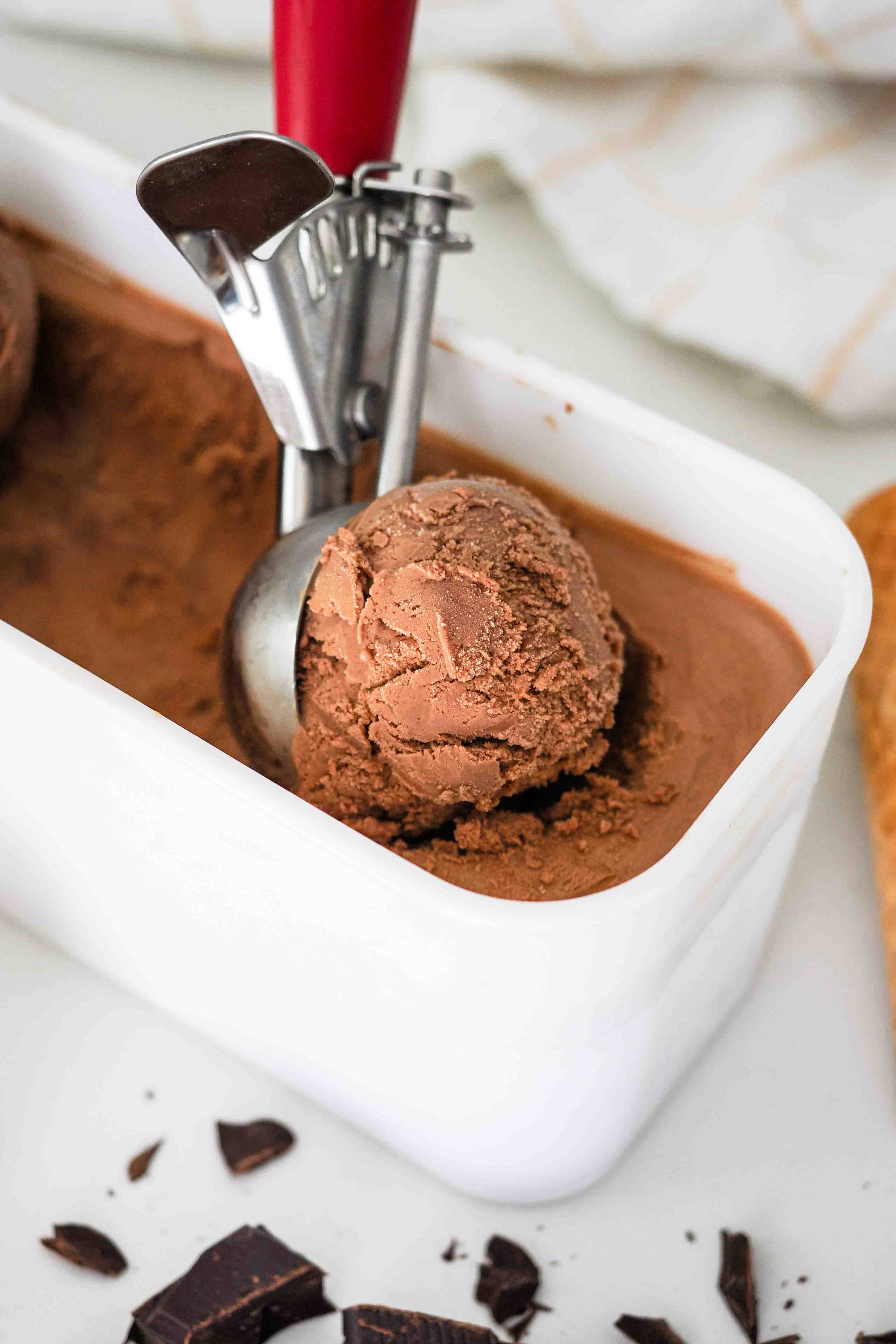 An ice cream scoop in a container of chocolate ice cream