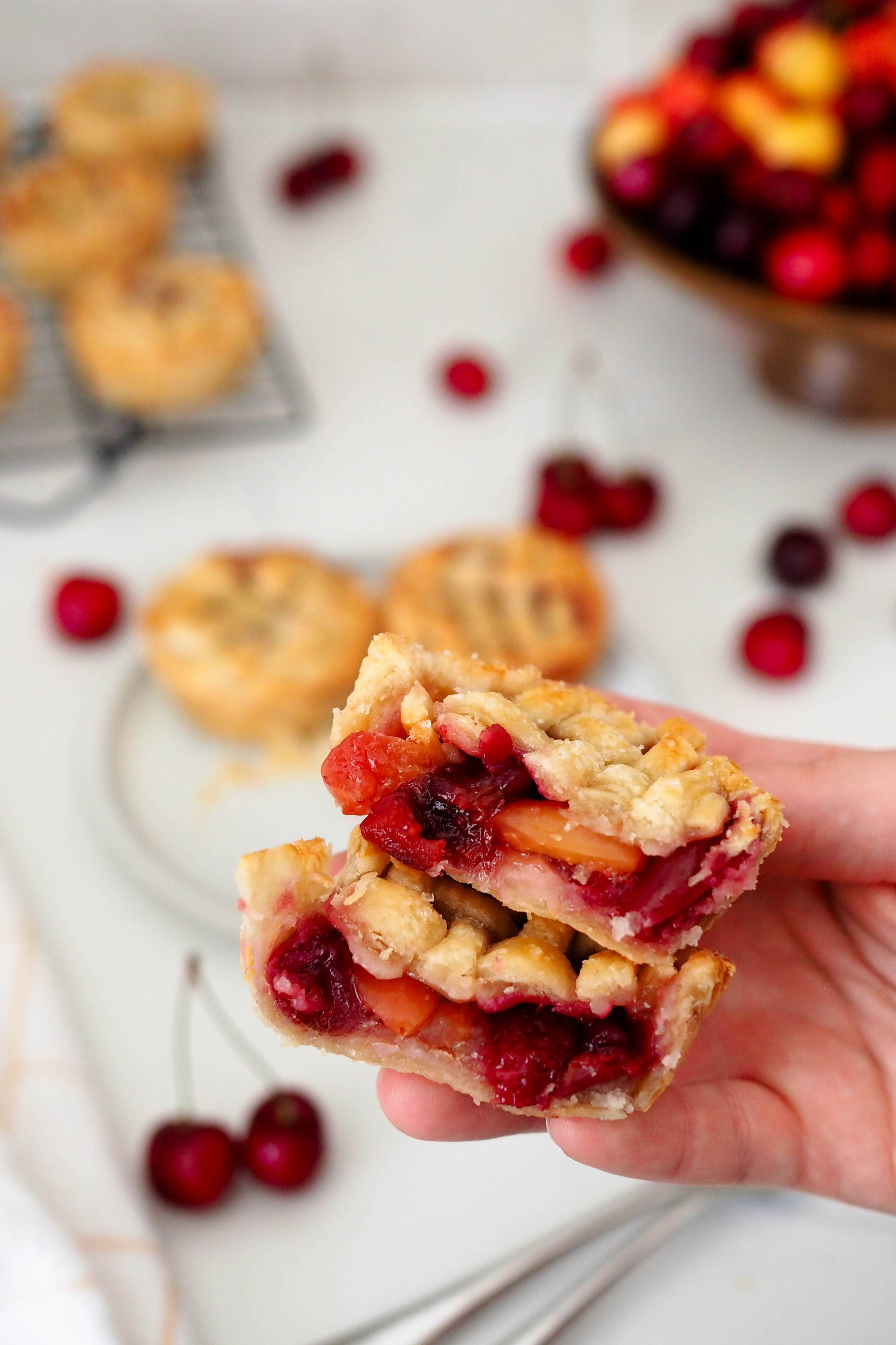 A hand holds up two halves of a mini cherry pie