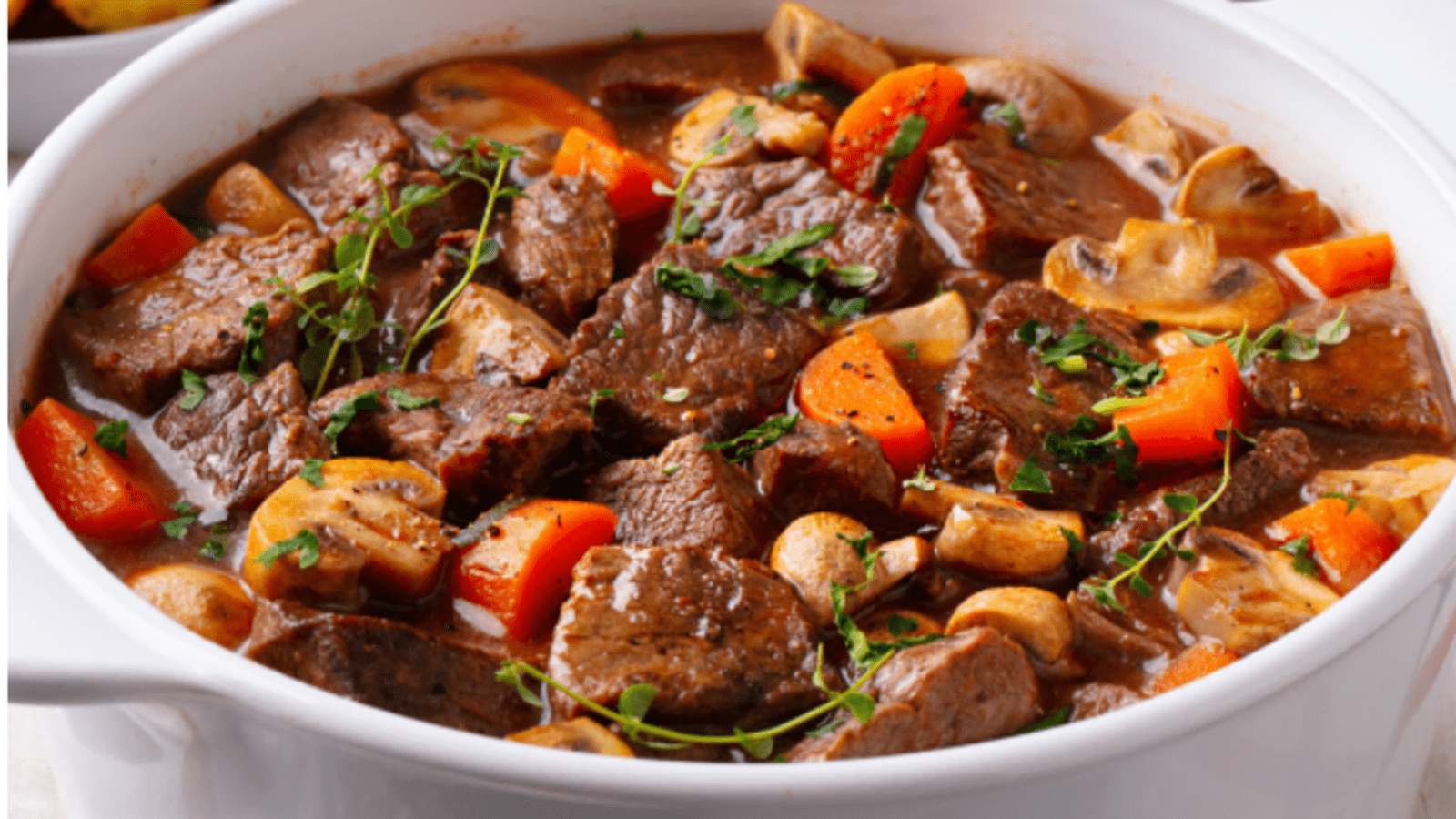 A hearty beef stew with chunks of meat, carrots, and potatoes, garnished with herbs.