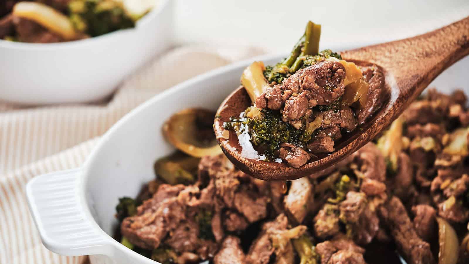 A hearty meat and vegetable stew being scooped out with a wooden spoon from a white casserole dish.