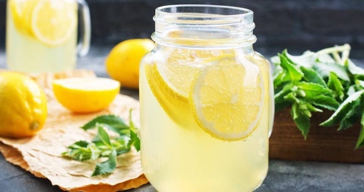 Lemonade in glass with mint in background.