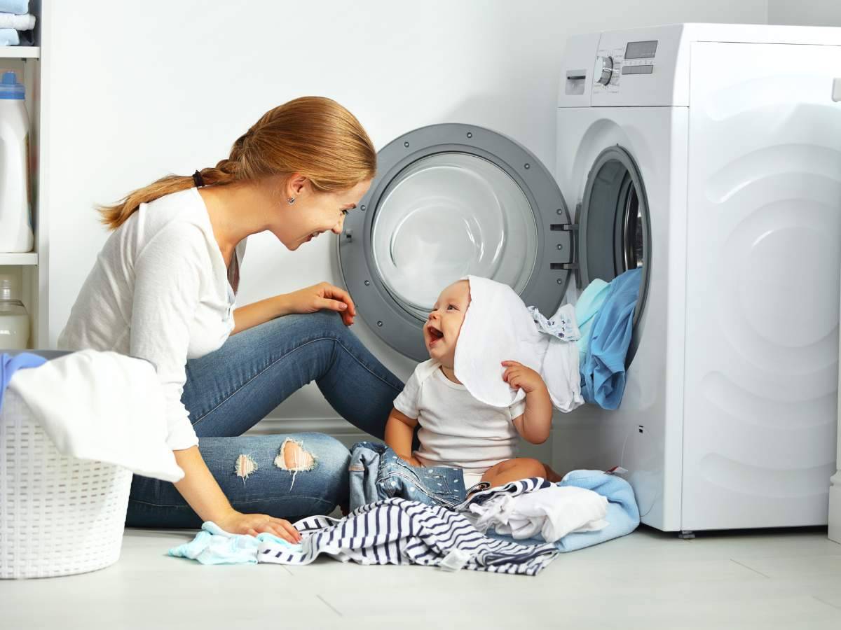 Mom and baby playing in front of an open laundry machine.