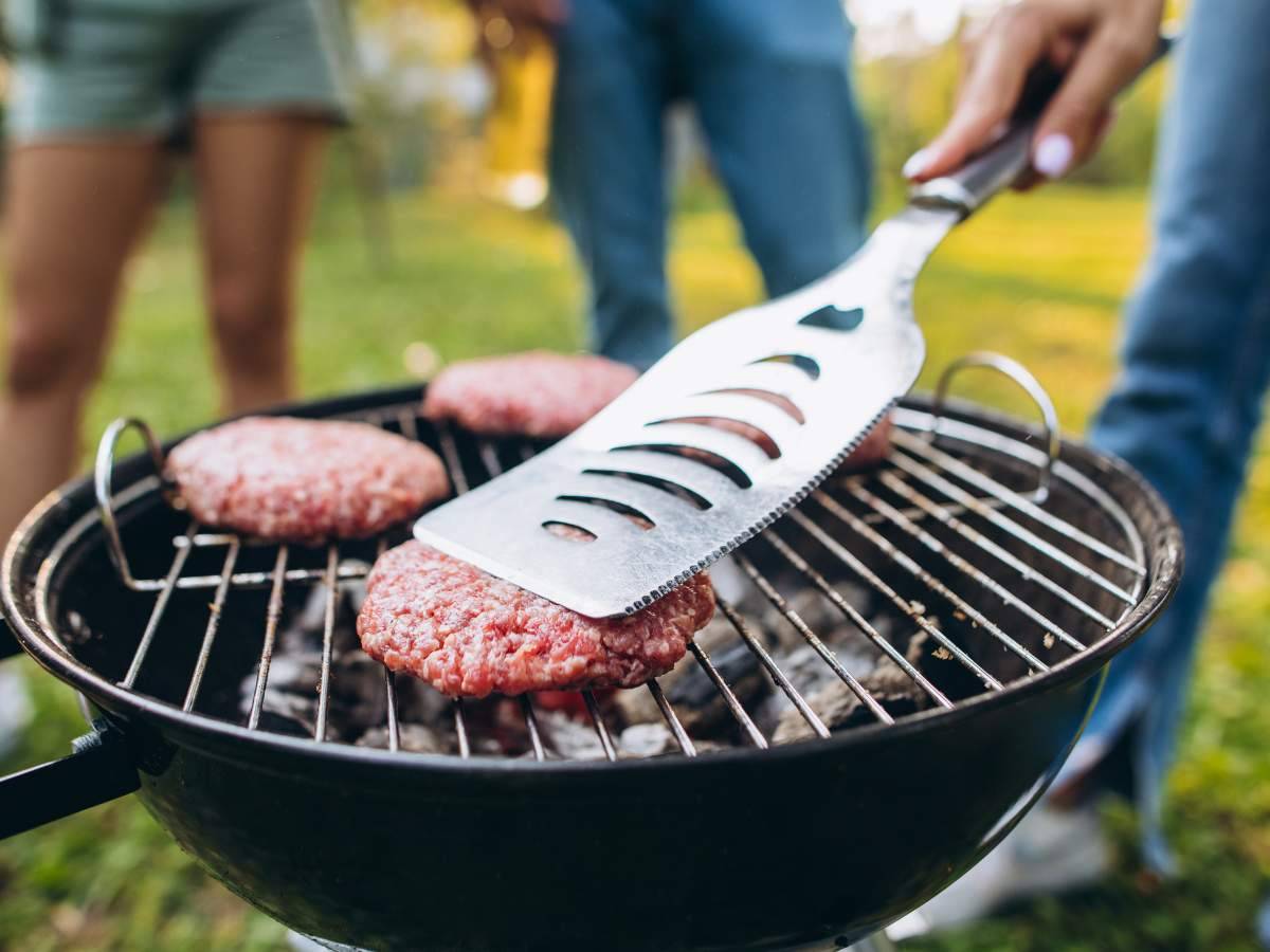 Three people are grilling hamburger patties on a charcoal grill. 