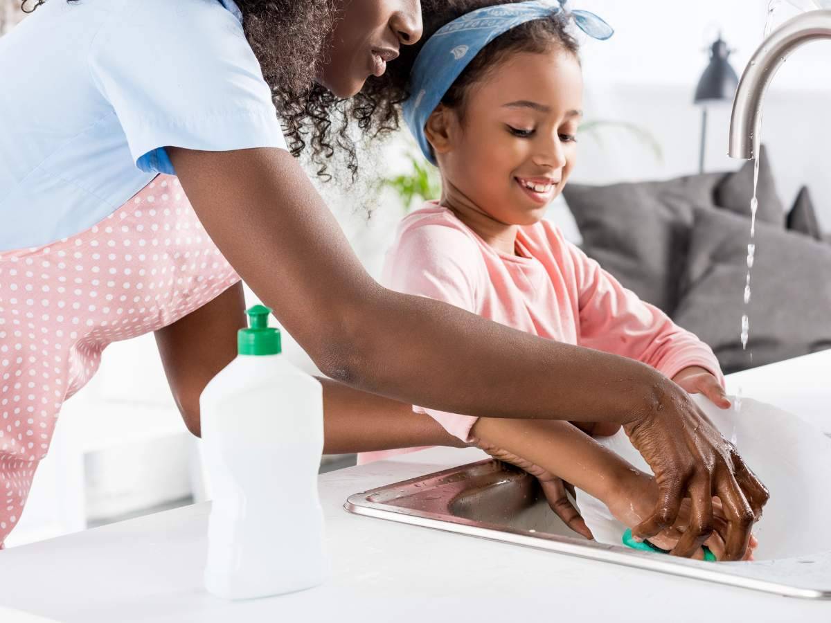 An adult and a child are washing dishes together at a sink.