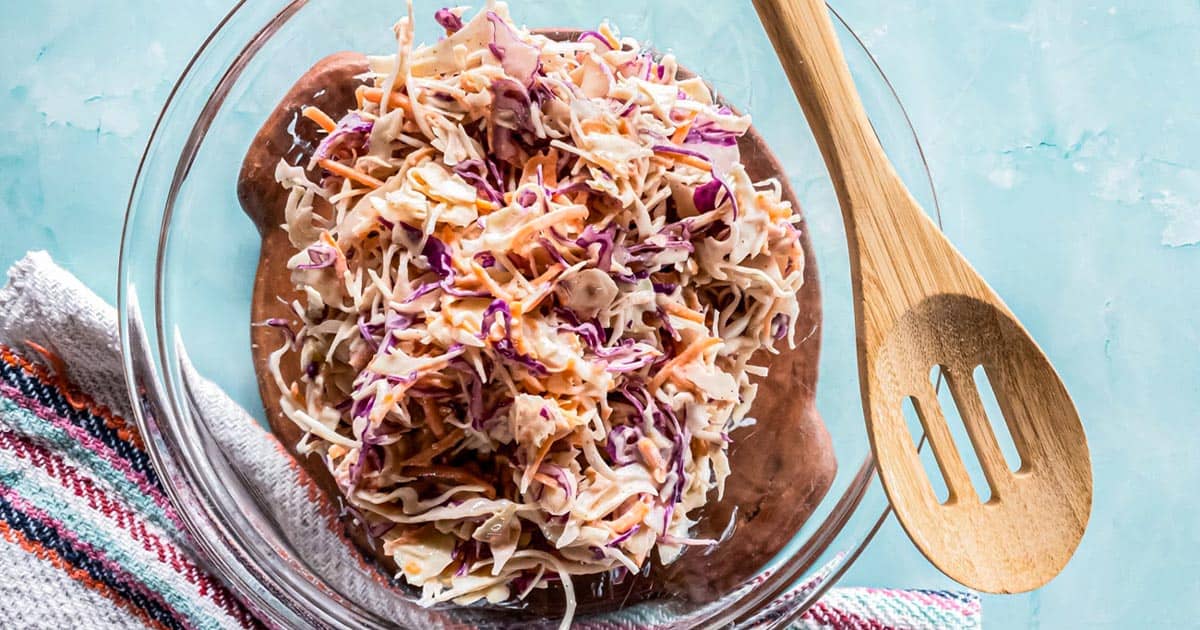 A picture of keto coleslaw in glass bowl with wooden spoon.