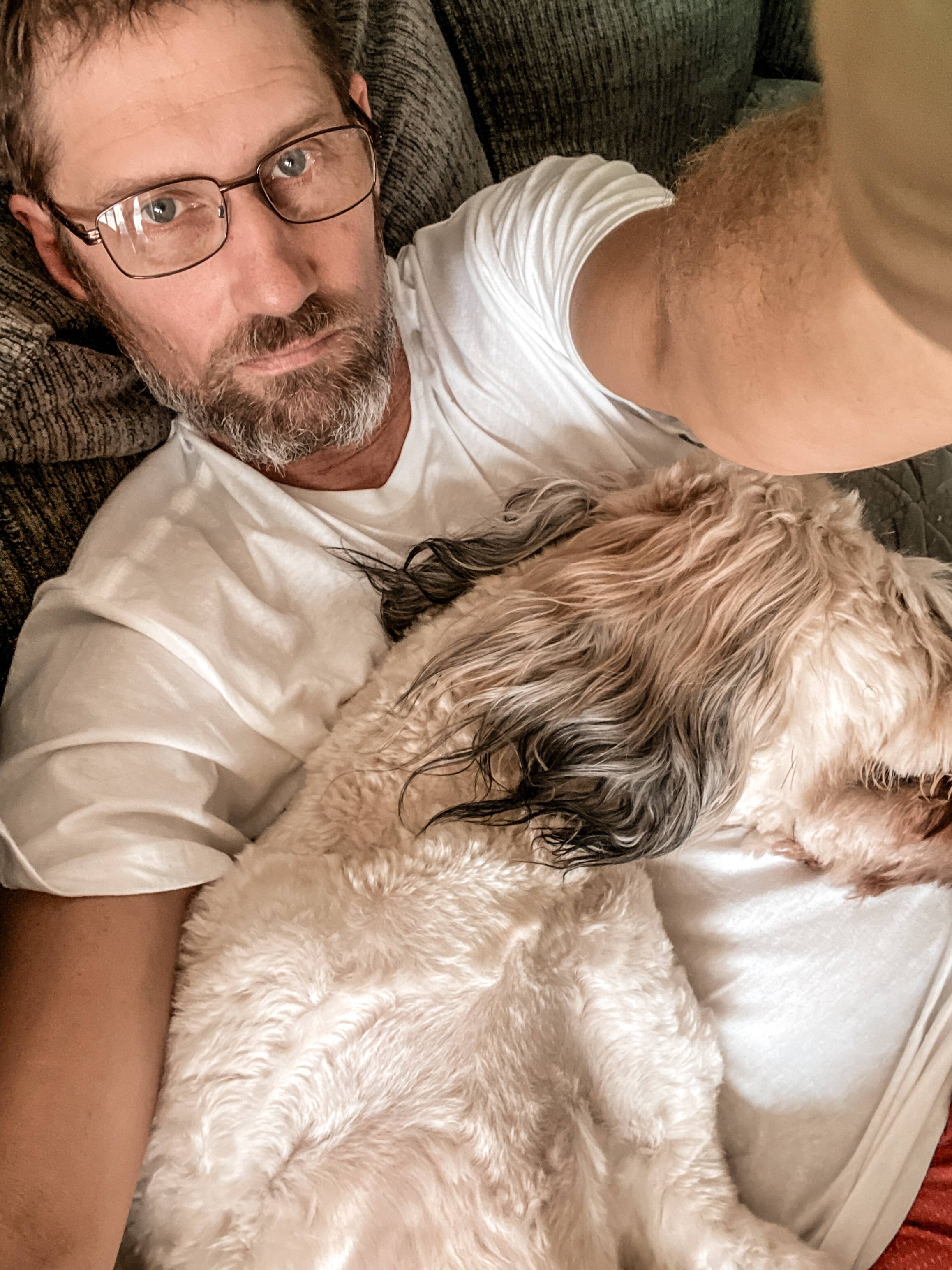 Image of Mister Mav with a grumpy face, cuddling with our goldendoodle Ember.