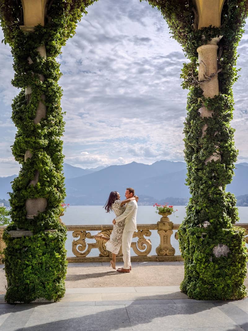 Couple embracing on a balcony overlooking a lake and mountains.