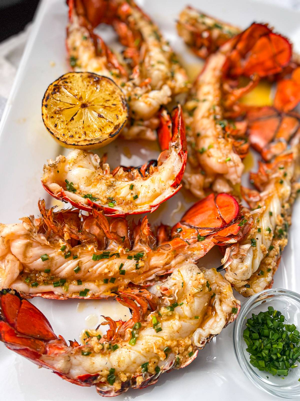 platter of grilled lobster tails with lemons, chives and garlic butter.