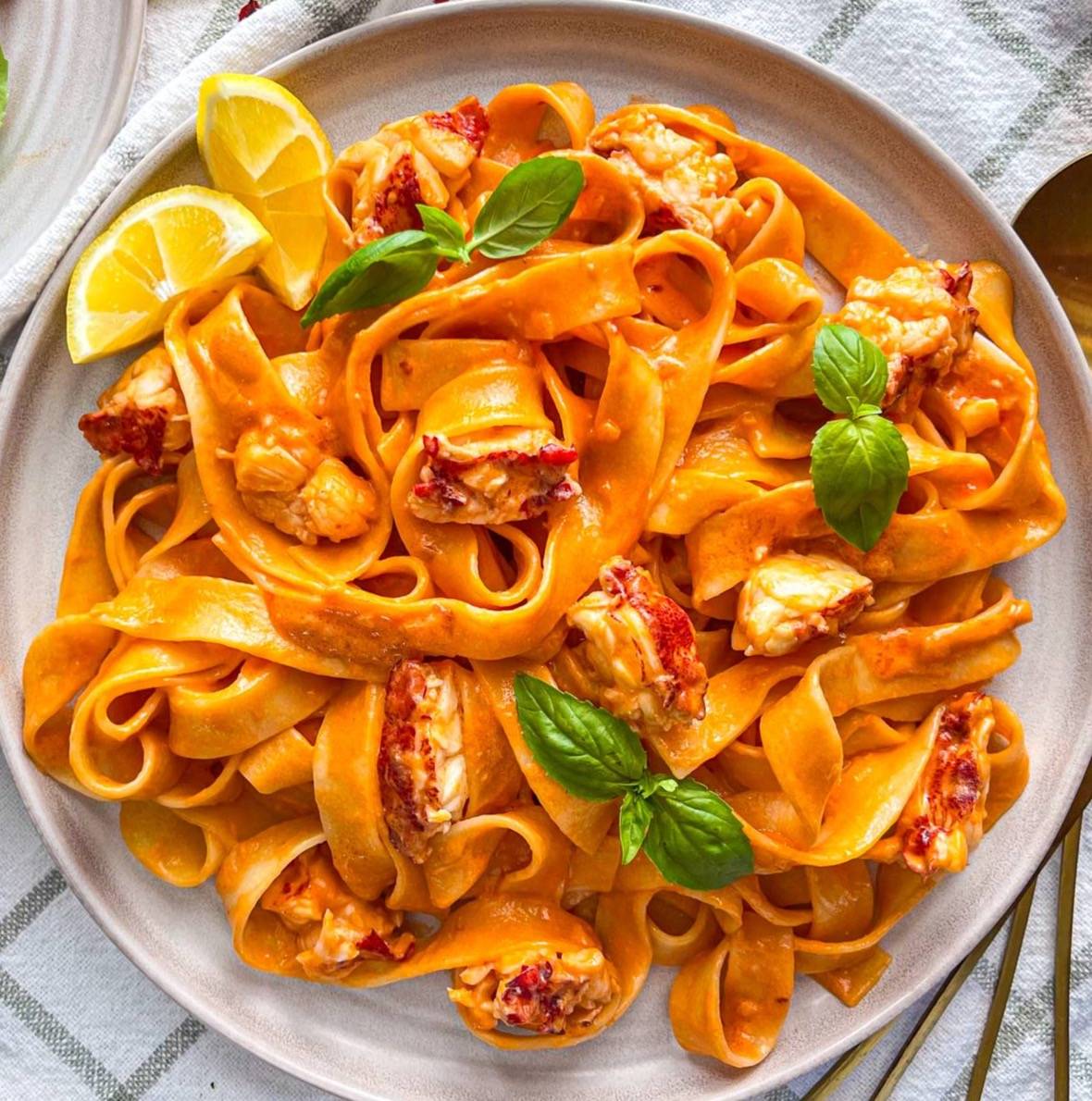 creamy tomato lobster pasta garnished with lemon wedges and fresh basil.