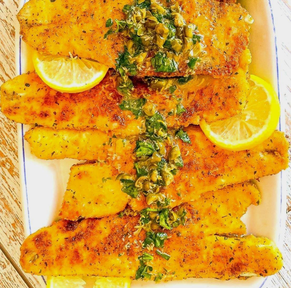 platter of crispy fish piccata garnished with lemons.