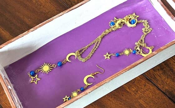A white tray with a purple bottom displays gold jewelry