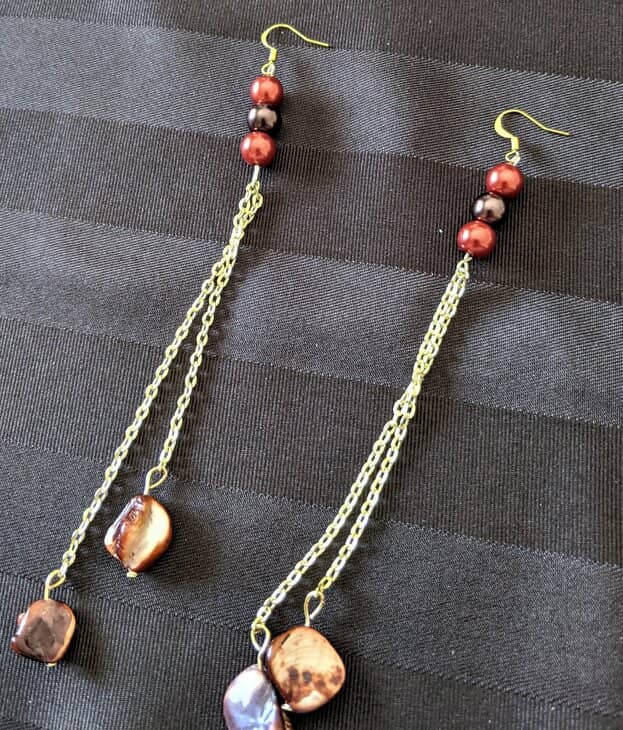 Two golden chain dangle earrings on a brown background.