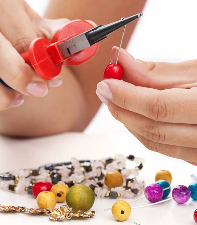 A person with pliers is working an assortment of beads and wires