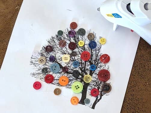 A picture of a black spindly tree, decorated with assorted sized buttons with different colors.
