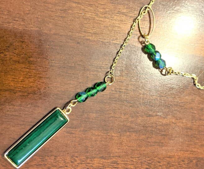 A gold chain with green beads and a pendant set on a wooden table.