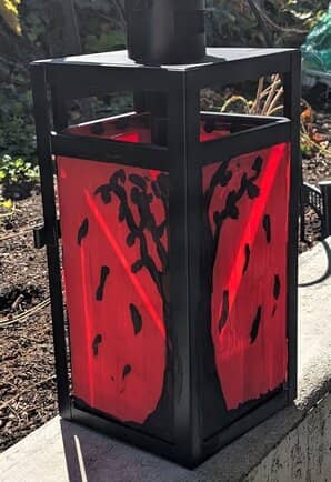A beautiful black and red fall lantern set on a sunny concrete patio wall.