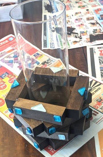 A plain glass vase with a dark stained wood base sitting on top of some newspapers.