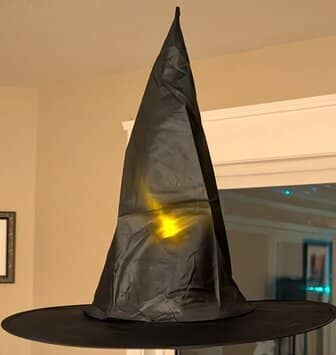 A black witches hat with a light hanging in a room.