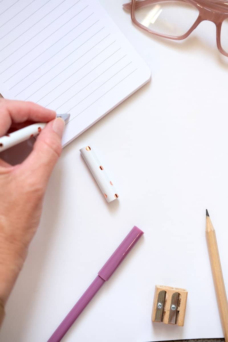 Hand writing in a notebook with pens and glasses.