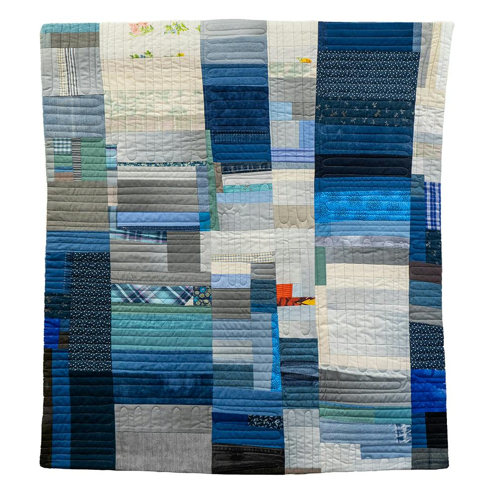 Photo of a patchwork quilt with fabrics in blue, gray, white, and a little yellow and orange