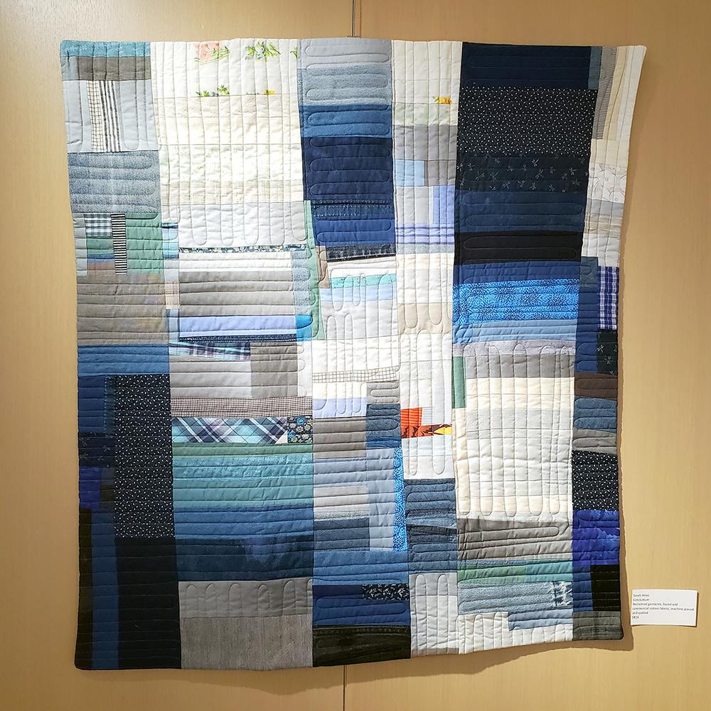 Photo of "Concludium," a patchwork quilt made by Sarah Atlee, displayed on a gallery wall.