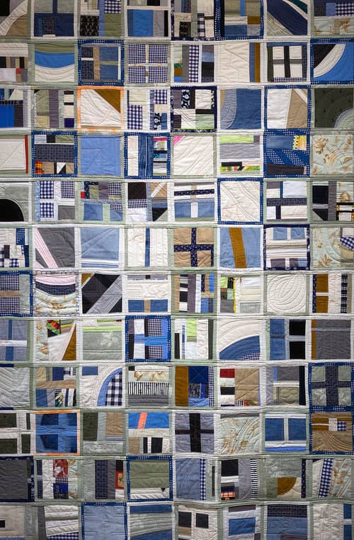 Closeup photo of a wall-hanging quilt, made from 108 individual squares. The quilt, mainly in neutral colors, has a geometric look.
