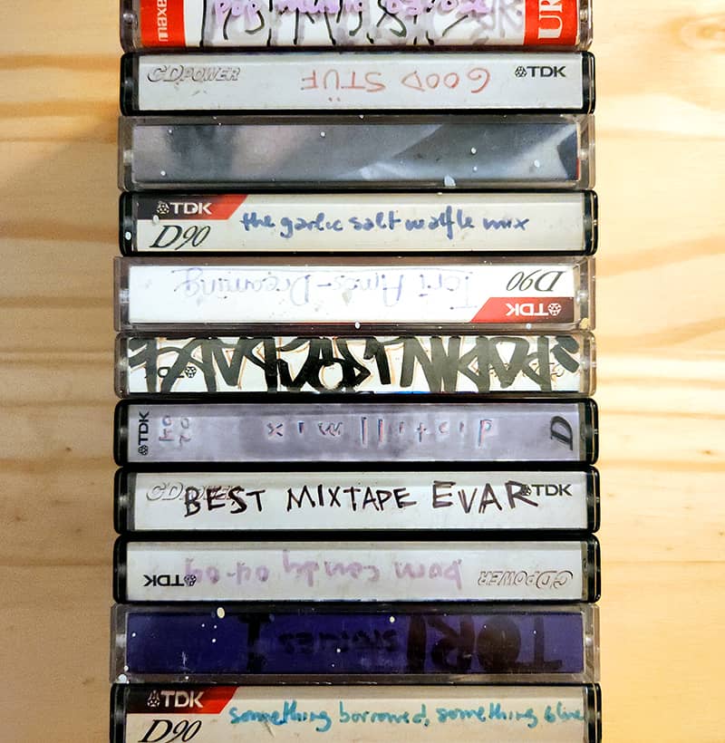 Photo of a collection of cassette tapes in their plastic cases. These are all homemade mix tapes with handwritten covers.