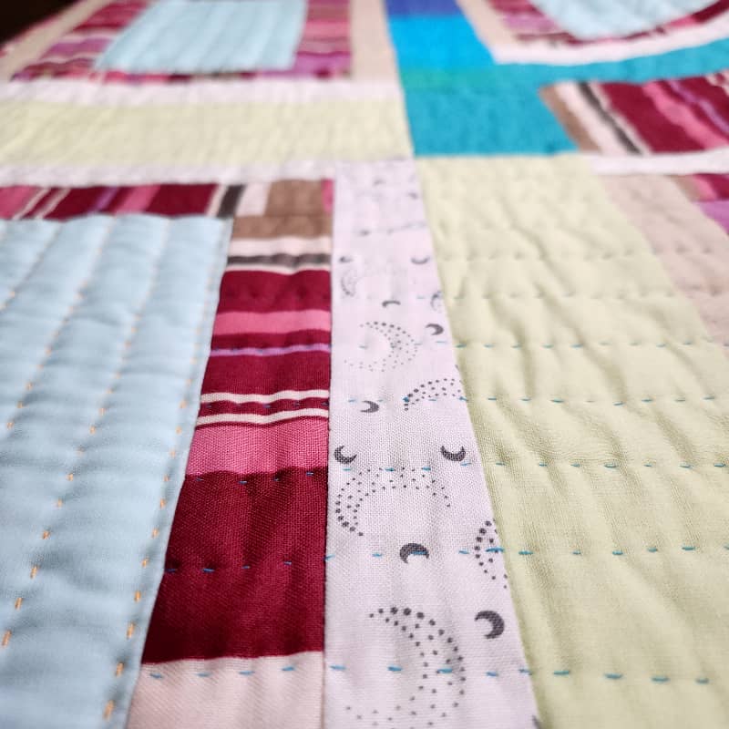 Detail view of California Baby. Here we can see strips of fabric in cyan, pale green, teal, and a maroon/pink stripe. Sarah's hand quilting stitches are visible.
