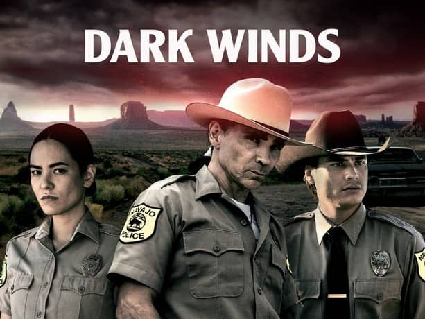 Promotional image for the TV series Dark Winds on the AMC+ streaming platform. Three figures dressed in police uniforms are set against a panoramic view of part of the Navajo Nation. Click image to view source on RottenTomatoes.com.