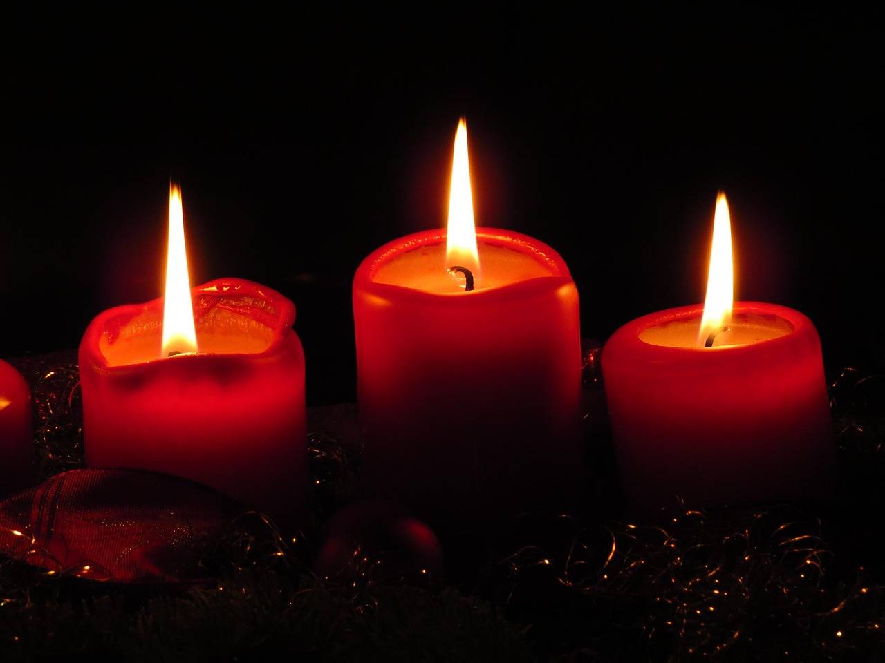 Photo of three red candles illuminating a dark red area. Public domain image.