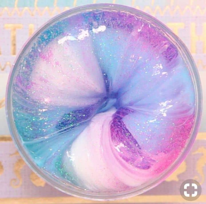 Photo of a circular container filled with fluffy slime. The slime has pink, blue, and purple pigment in it, as well as glitter.