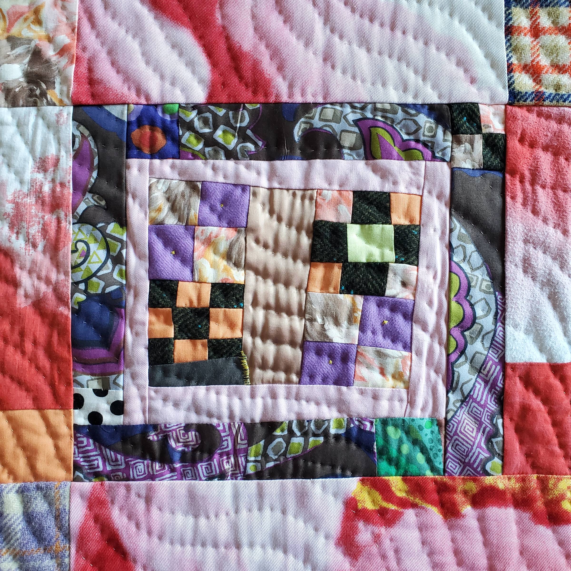 This is a detail of an improvisational patchwork quilt by Sarah Atlee. The design is a series of concentric rectangles, some subdivided into squares. The fabric colors include red, white, pink, orange, pale green, and many shades of purple. In this photo the texture created by hand quilting is visible.