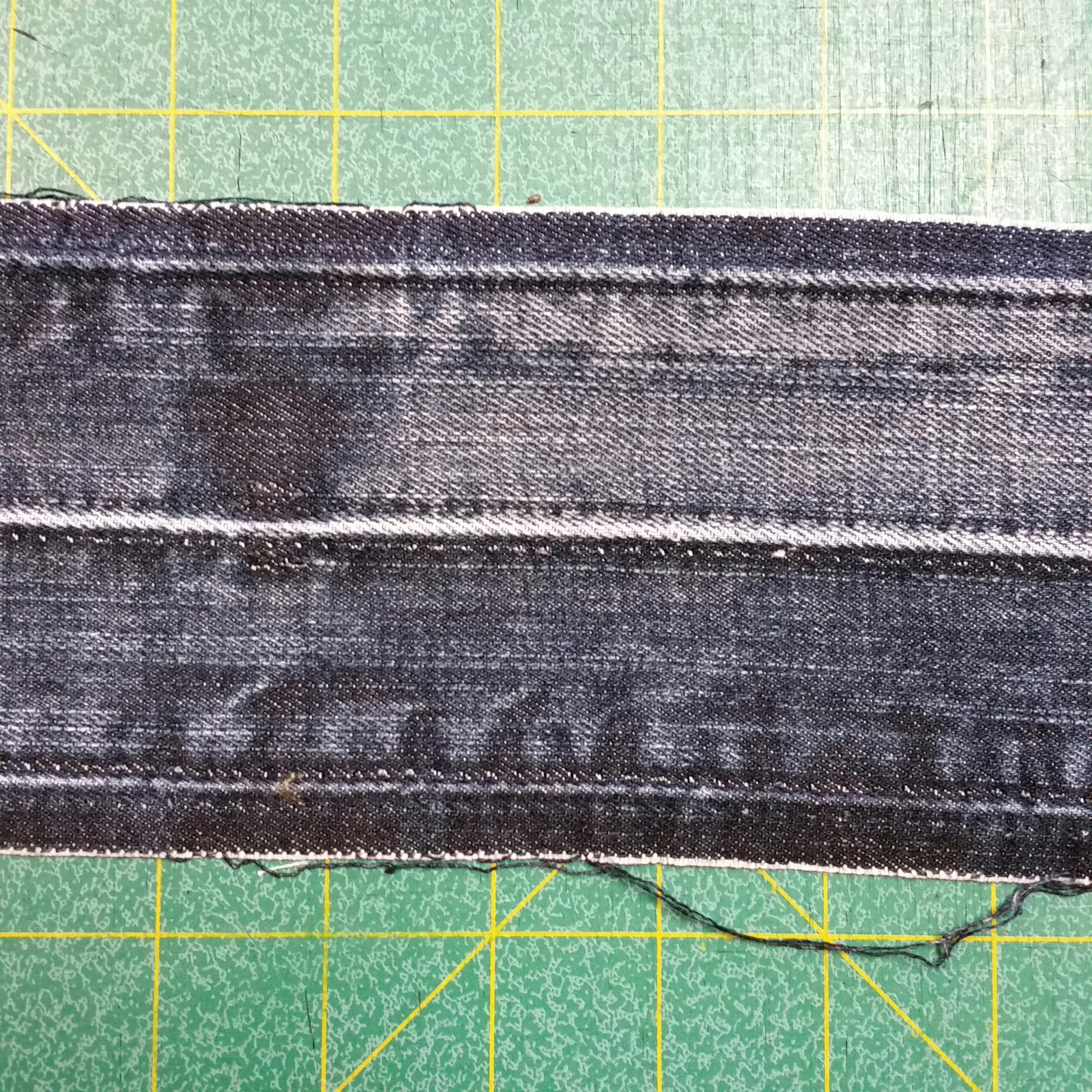 Photo of part of a waistband taken from a deconstructed pair of jeans. It's sitting on a green cutting mat with a yellow one-inch grid.